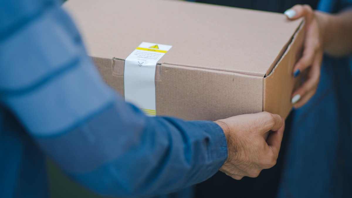 A person taping shut a cardboard shipping box on a table, preparing a package for return or delivery