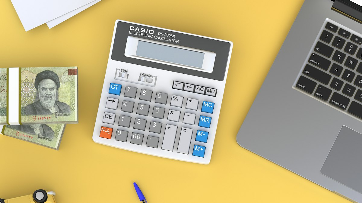 A calculator and laptop on a desk next to papers, set up for working through pricing figures