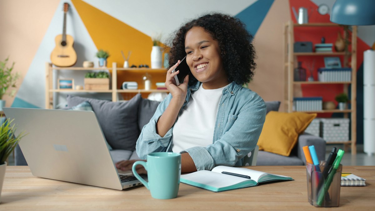A woman at an office desk talking on the phone while working on a laptop, representing a fundraising or donor relations call