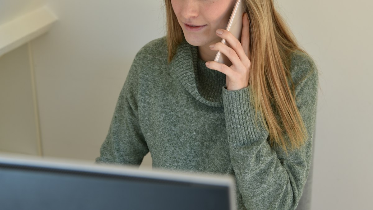 A staff member at a desk talking on a cell phone while looking at a computer screen