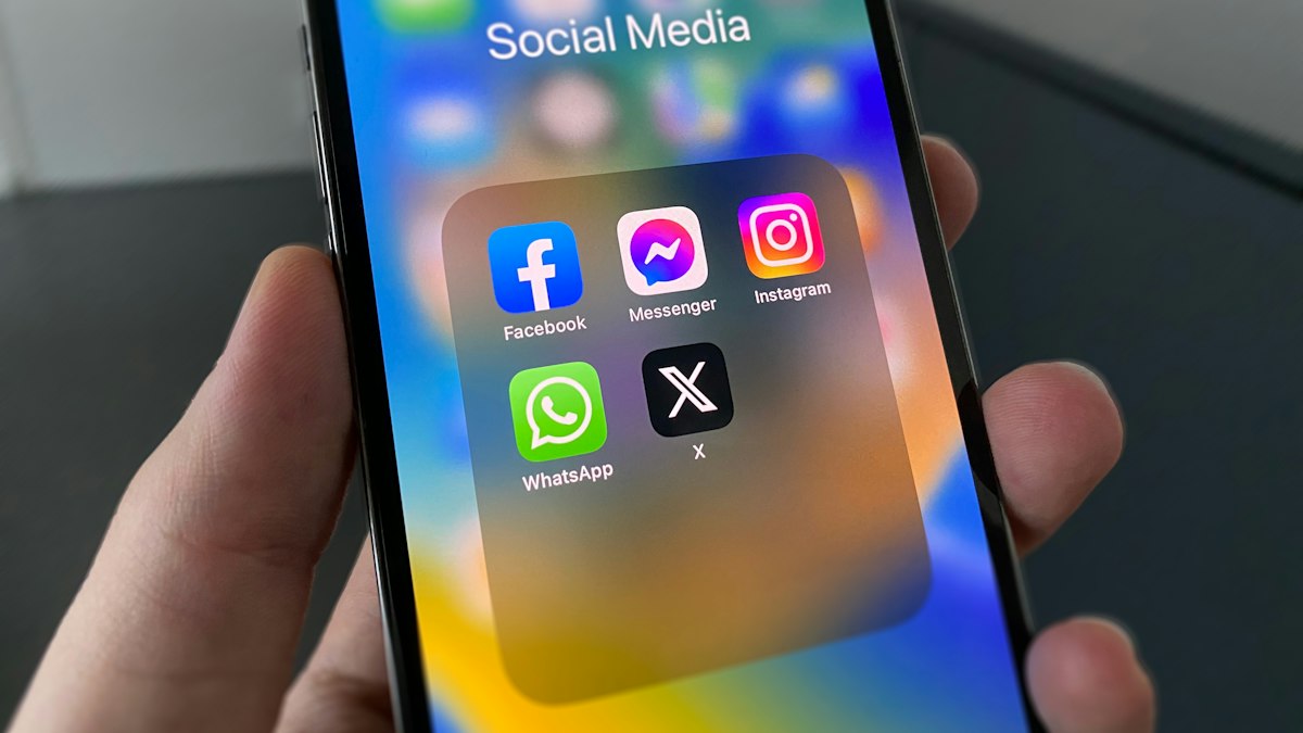 A person holding a smartphone showing social media app icons on the screen