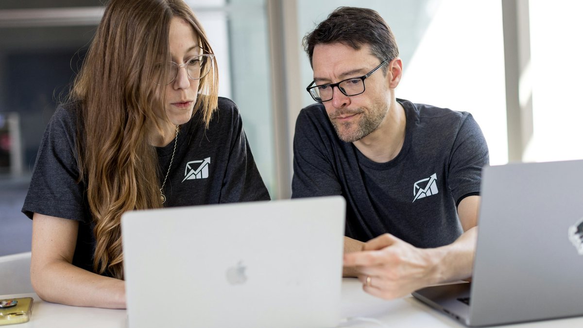 Two colleagues sitting side by side at a laptop in a bright office, reviewing work together, representing a team using an internal AI copilot inside the tools they already have open