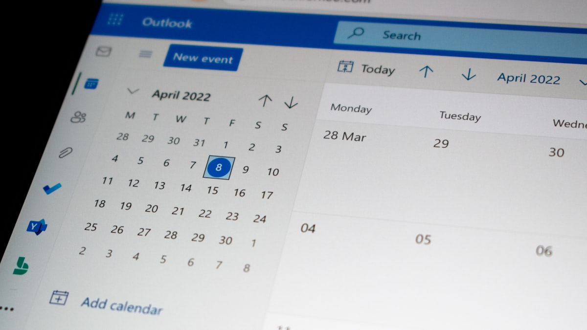 A desk with a laptop open to a calendar app, a pen, and a phone nearby, representing the scheduling systems a voice agent has to integrate with
